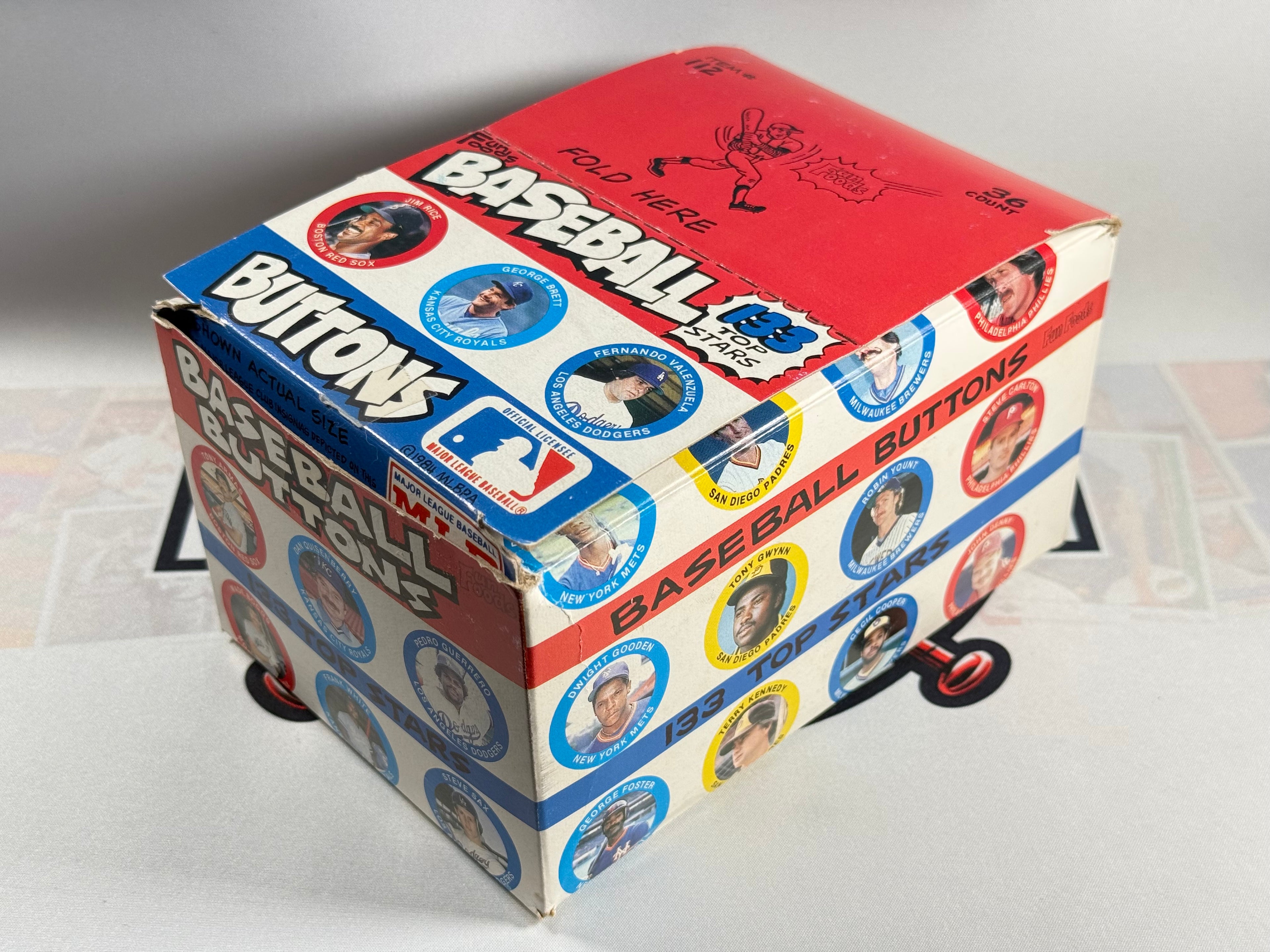 Box of baseball buttons with colorful design on a light background