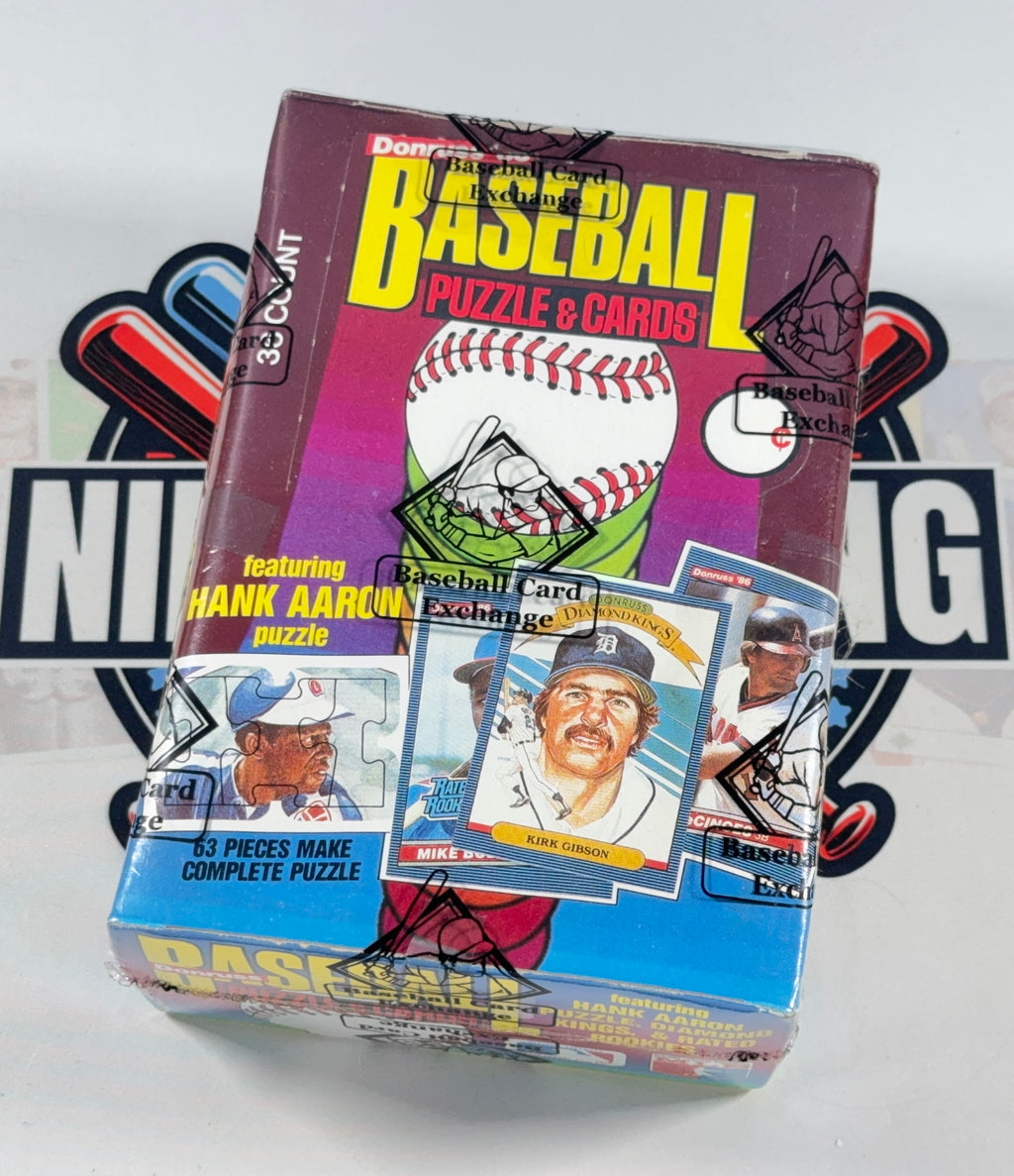 A vintage 1986 Donruss Baseball Puzzle & Cards box, featuring Hank Aaron and signed autographs on the front, displayed on a white background with a blurred logo behind it.