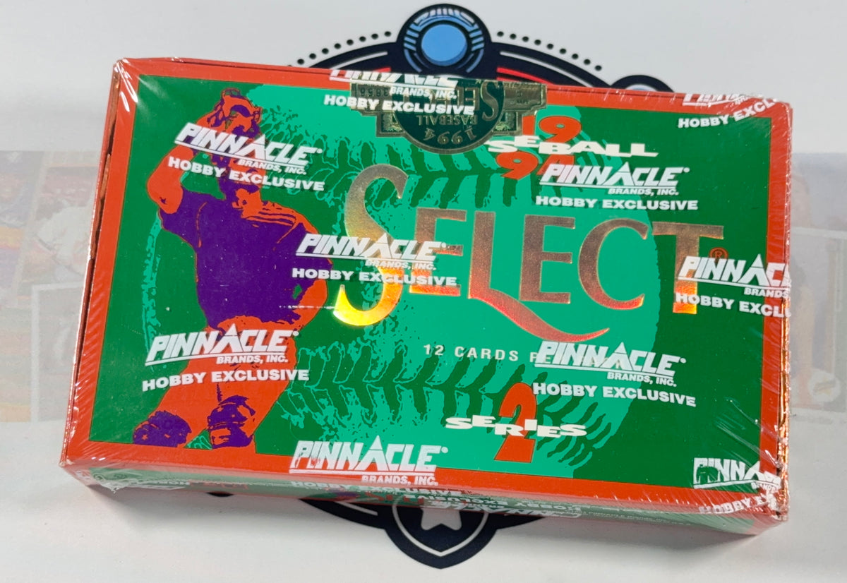 A sealed Pinnacle Select Hobby Exclusive card box with a green front, orange border, and multicolor graphics, photographed on a white surface with a black circular stand visible behind it.