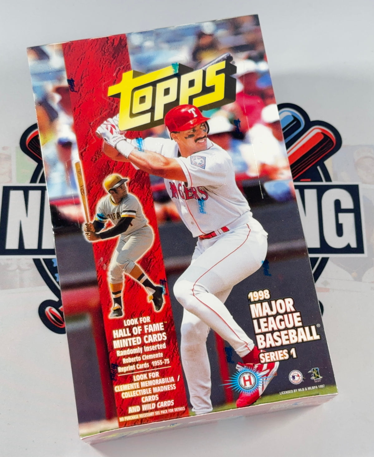 A Topps 1998 Major League Baseball Series 1 card booster box shown standing upright on a white surface with a blurred branded backdrop.
