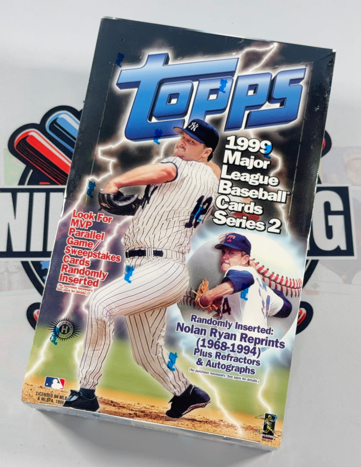 A boxed Topps 1999 Major League Baseball Cards Series 2 trading card box, photographed at an angle against a light background with a blurred baseball graphic behind it.