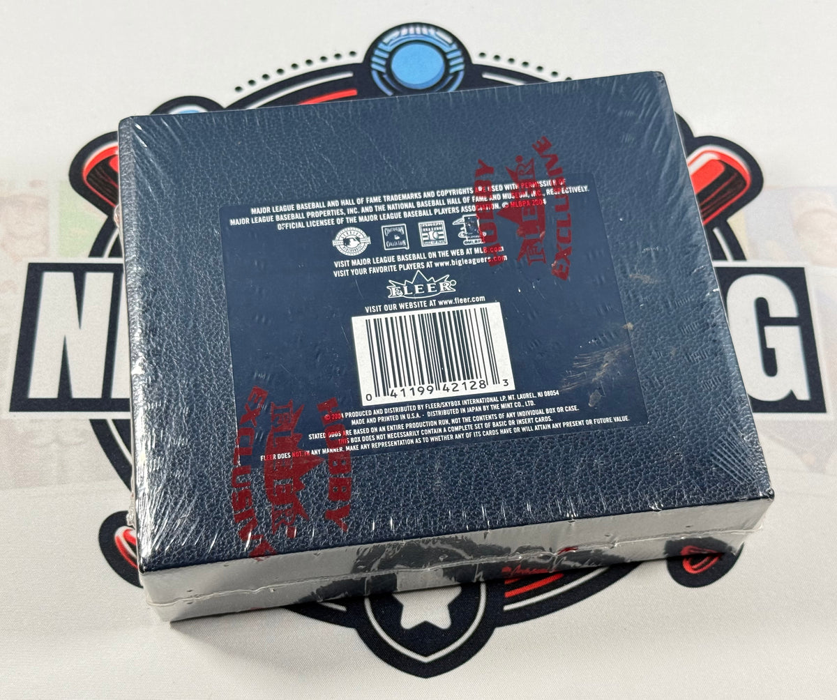 A sealed dark blue box with a barcode label and red printed markings, photographed from above on a white surface with a large black-and-red graphic behind it.